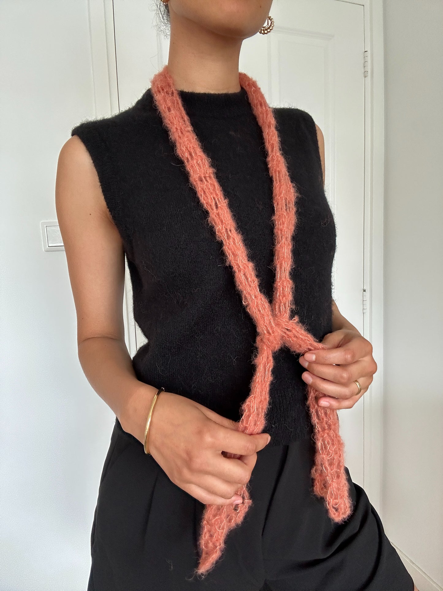 Shows a model wearing our crocheted, peach colored, thin yet fluffy 'anna' scarf. Made by The Woollers