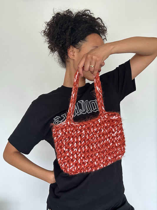 Shows a model holding a crocheted blood orange red and rose pink FLUFFY LINT Handbag. Made by The Woollers