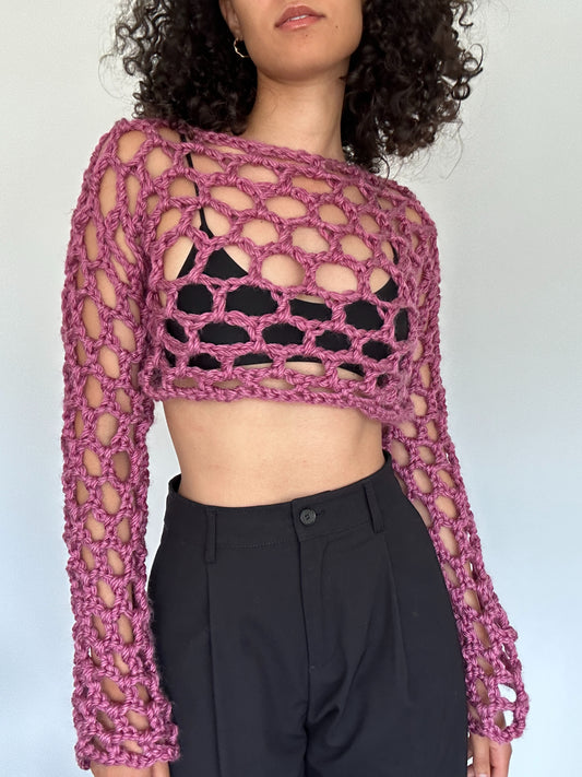 Shows a model wearing the crocheted KNOTTY Long Sleeve Crop Top, which is pink and has an open mesh design