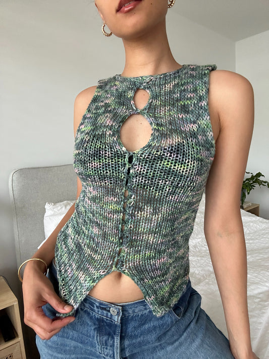 It shows a model wearing our knitted izzy tank top which has various shades of green and pink. The top has multiple open sections in the front. Made by The Woollers