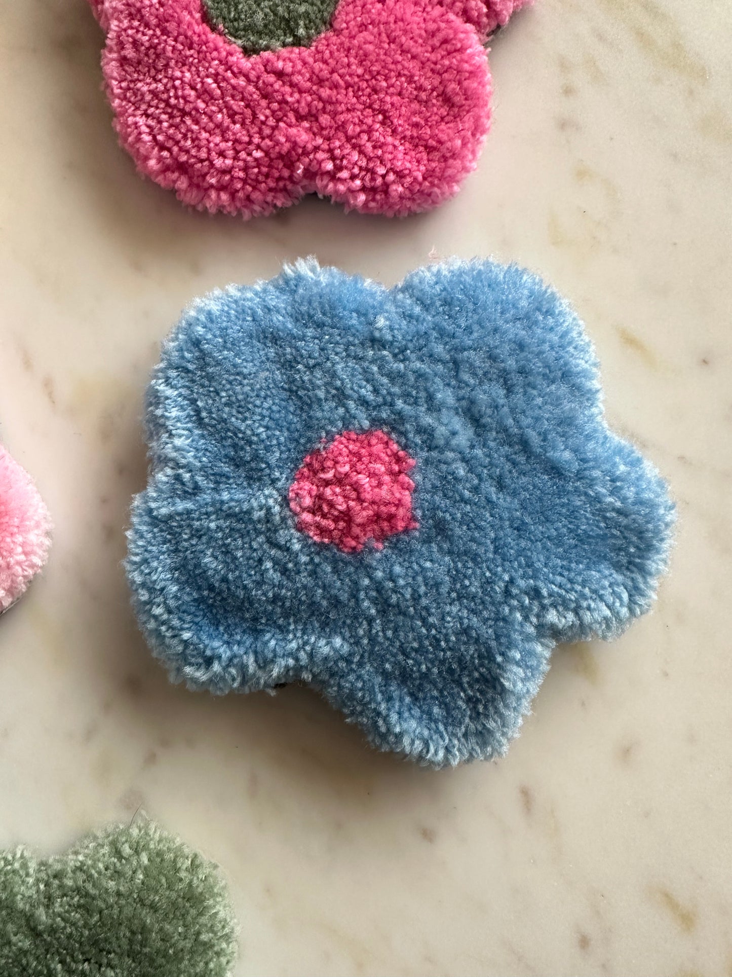 Shows one of our tufted flower coasters with blue petals and a pink core. Made by The Woollers