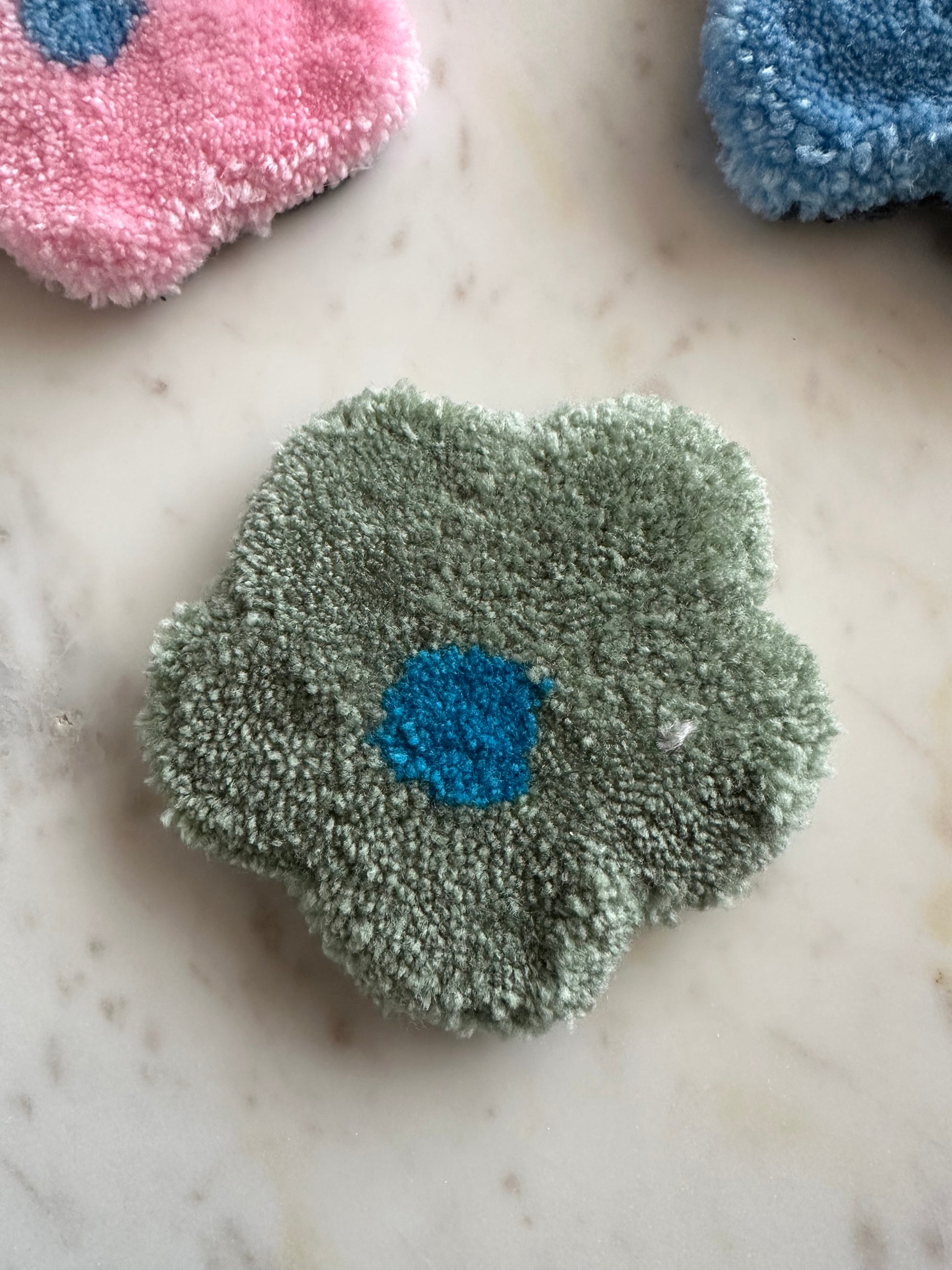 Shows one of our tufted flower coasters with green petals and a blue core. Made by The Woollers