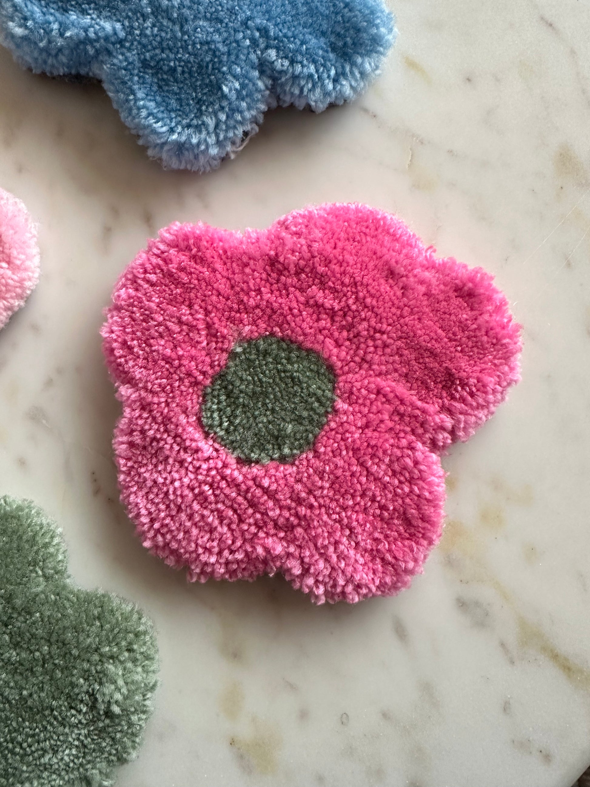 Shows one of our tufted flower coasters with pink petals and a green core. Made by The Woollers