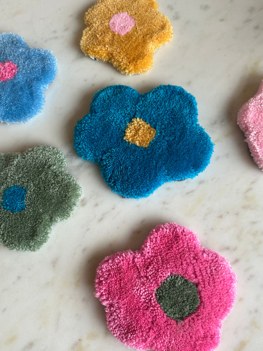 Our tufted flower shaped coasters placed on a table in various color combinations, such as green and blue, pink and green, yellow and pink. Made by The Woollers