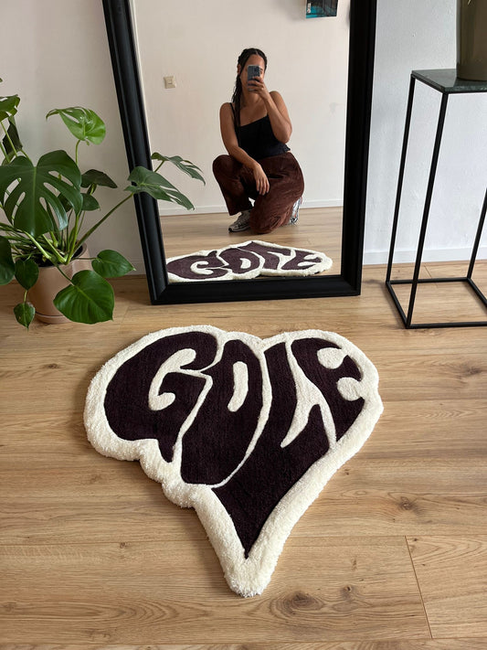 Shows a tufted heart shaped white and brown rug with the text 'GOLF' in it. Made by The Woollers