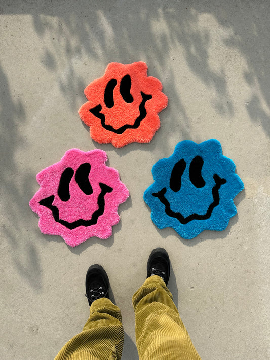Shows three variants of our tufted TRIPPY SMILEY Rugs, in colours popping pink, ocean blue and peachy orange. Made by The Woollers