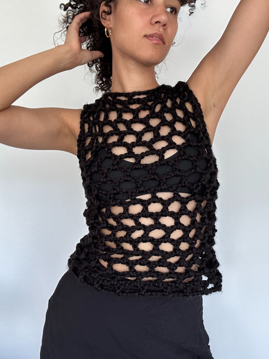 Shows a model wearing the KNOTTY Tank Top, which is a crocheted black open mesh tank top made by The Woollers