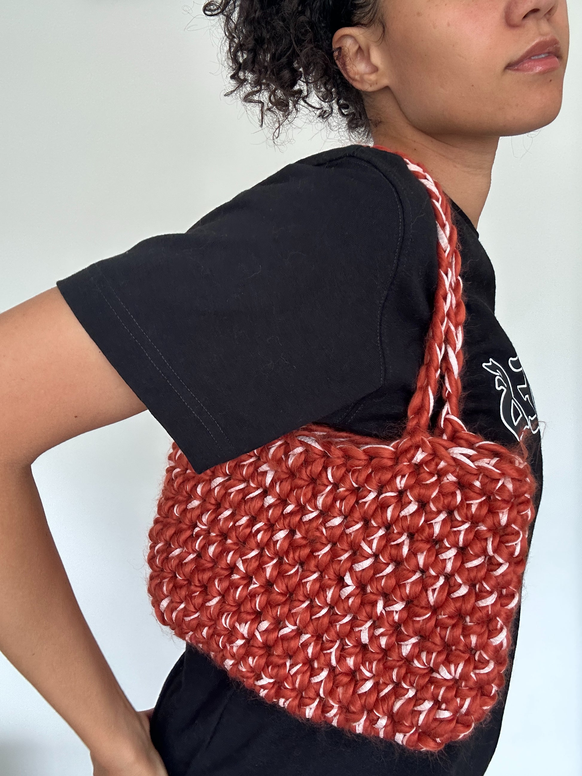 Shows a model wearing a crocheted blood-orange red and rose pink FLUFFY LINT Handbag over her shoulder. Made by The Woollers