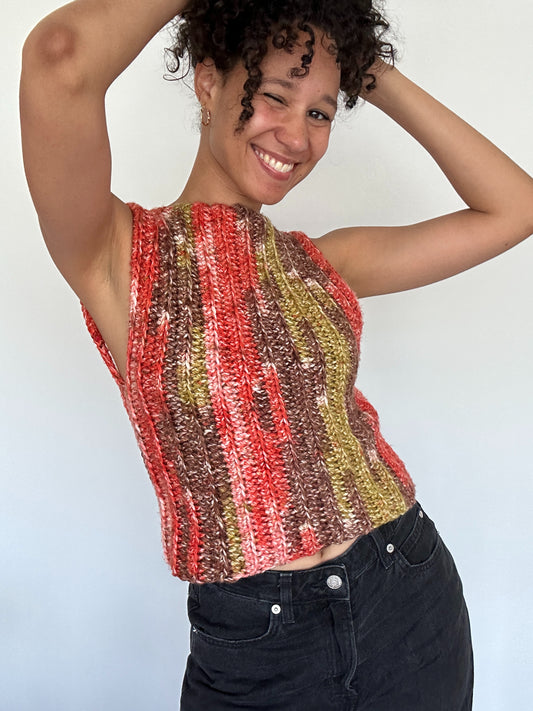 Shows a model wearing the crocheted NORA Open Back Top, which has a low cut open back and covered front in the colors brown, green and orange. Made by The Woollers