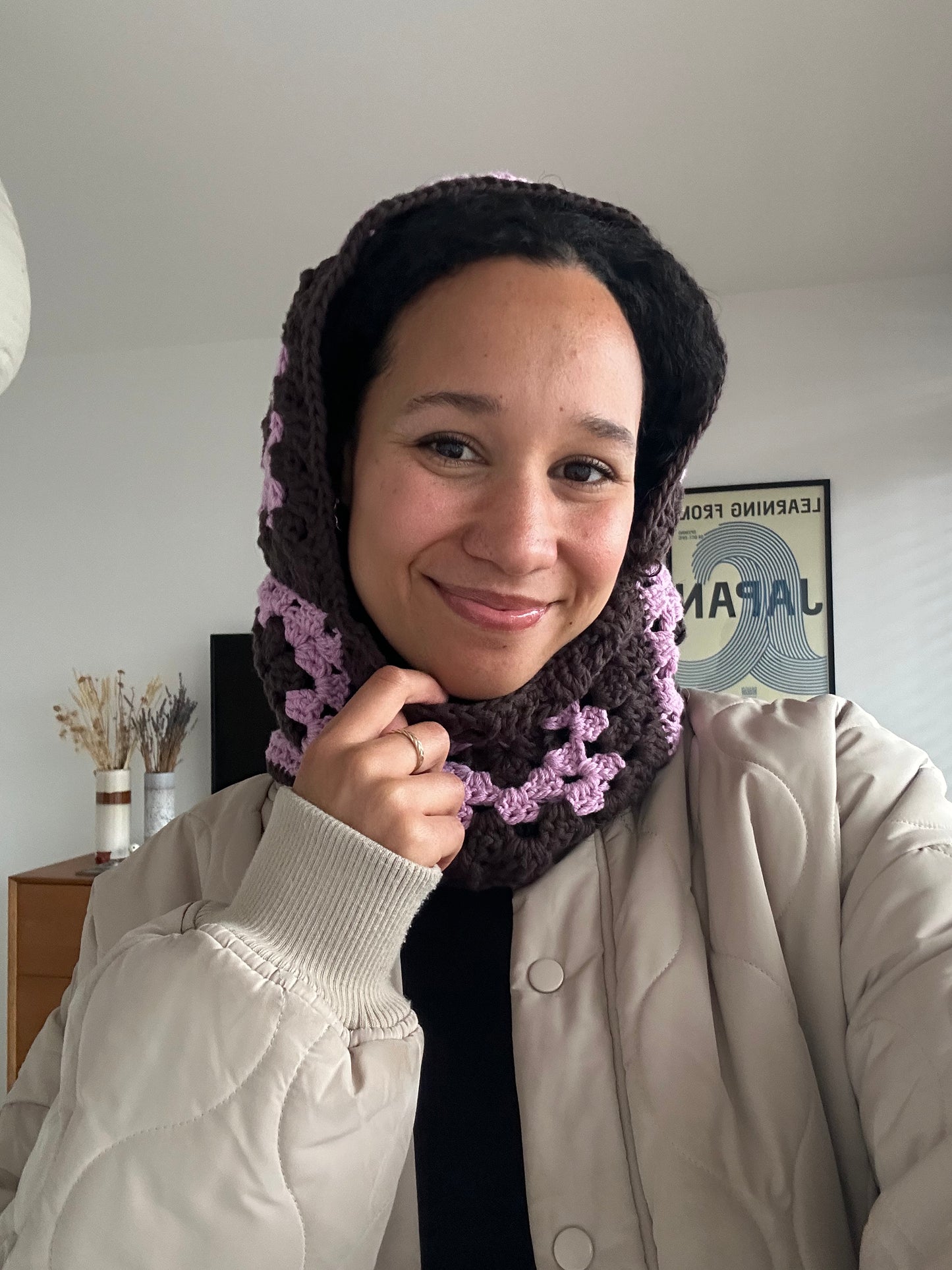 Shows a model wearing the crocheted umi balaclava which is made of pink and brown granny squares. Made by The Woollers