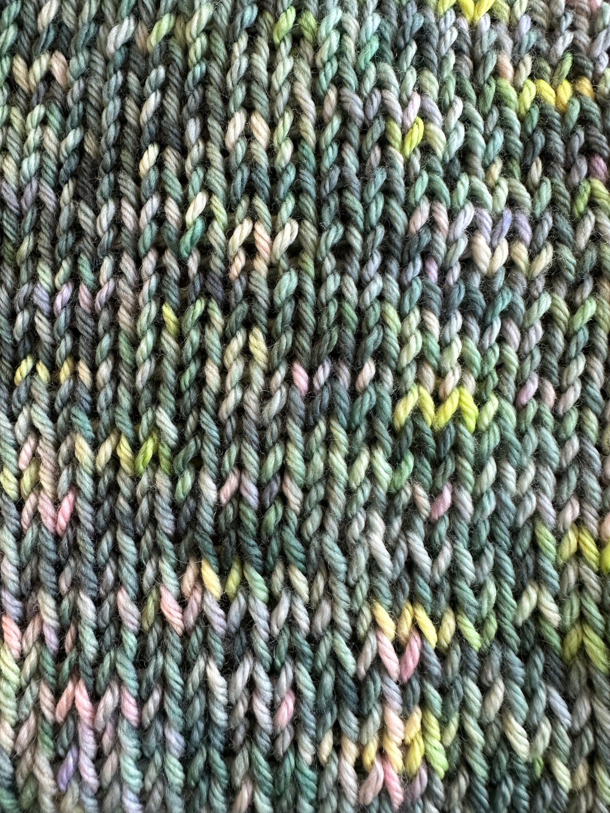 Shows a close up of the texture and pattern of the knitted tank tops 'iris' and 'izzy'. It shows various hues of green, pink and blue. Made by The Woollers