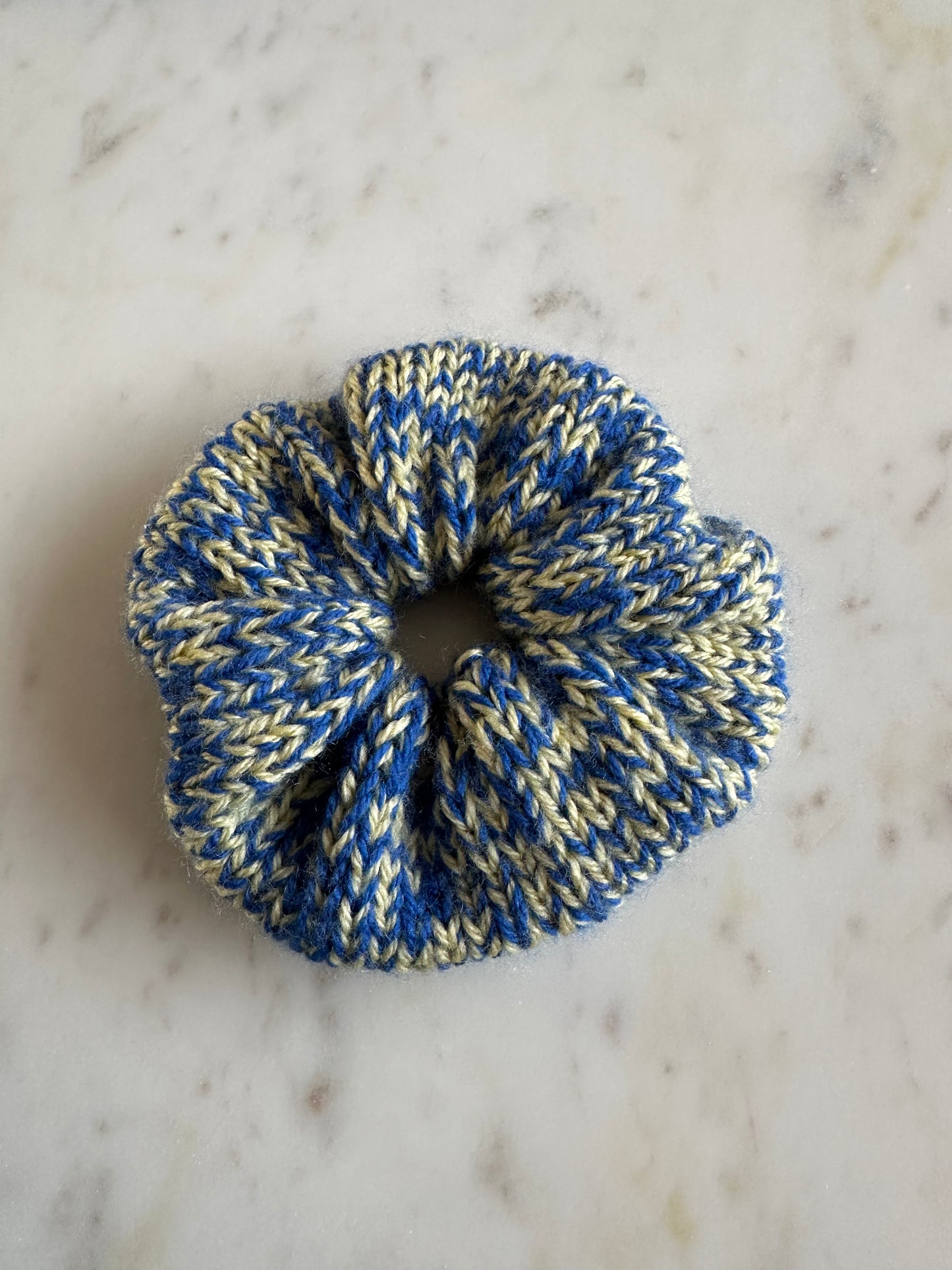 The image shows a knitted scrunchie in a mix of yellow and blue yarn. Made by The Woollers