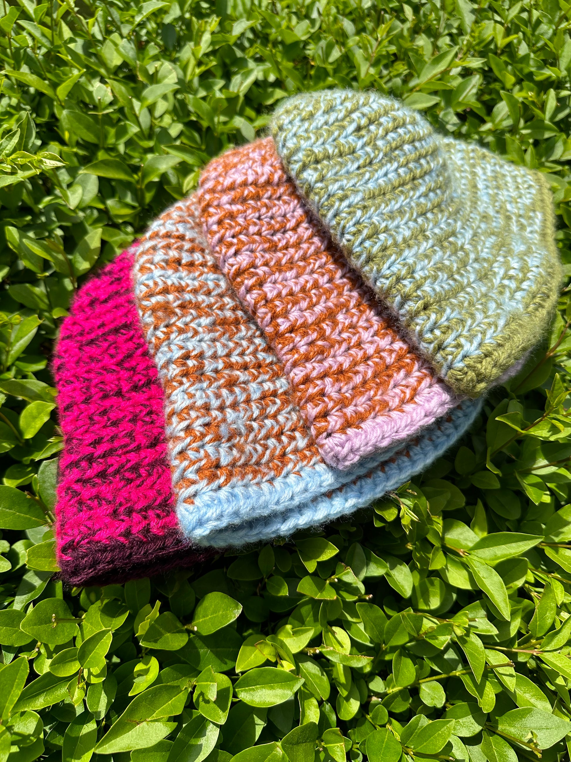 Shows a range of crocheted MOMI Buckethats in color combinations of pink and purple, blue and orange, lila and orange, and green and blue