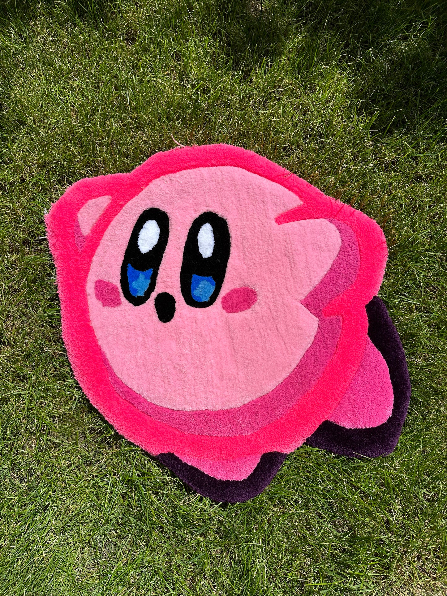 Shows our tufted KIRBY Rug, it's a bright pink round shaped rug which portrays the iconic Nintendo character Kirby