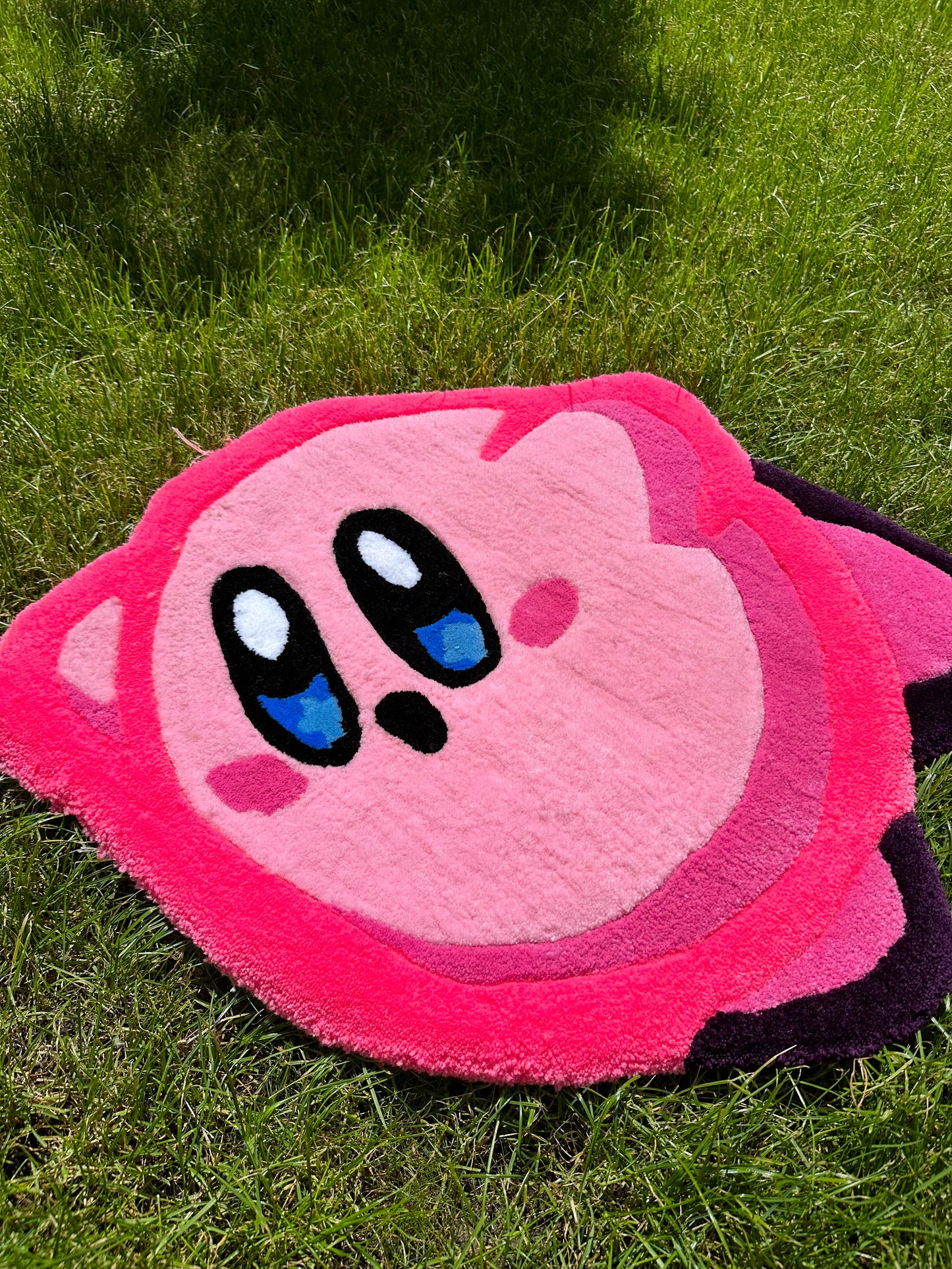 Shows our tufted KIRBY Rug, it's a bright pink round shaped rug which portrays the iconic Nintendo character Kirby