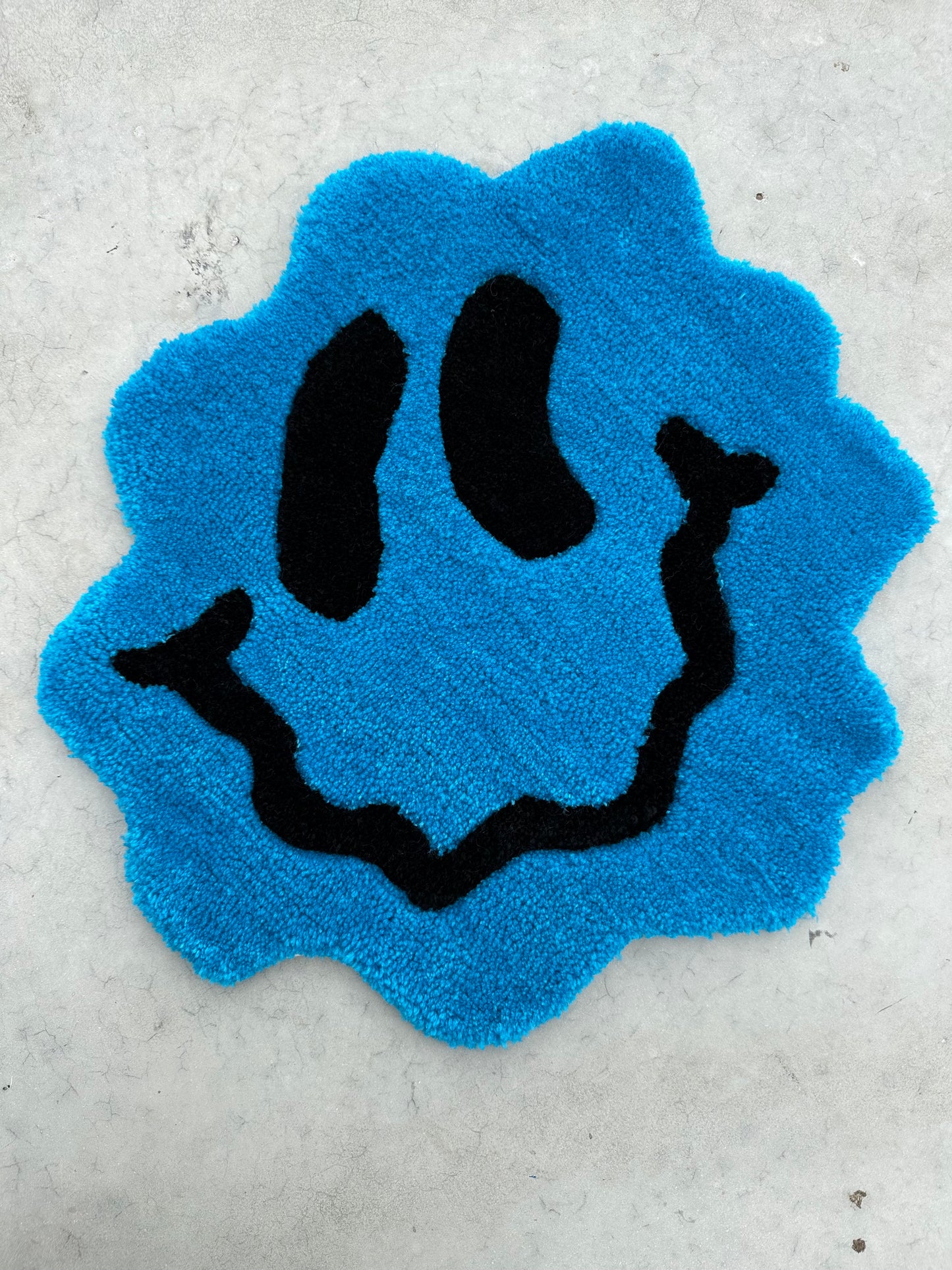 Shows our tufted TRIPPY Smiley Rug, it's a small blue hued smiley face with curvy edges and lines. Made by The Woollers