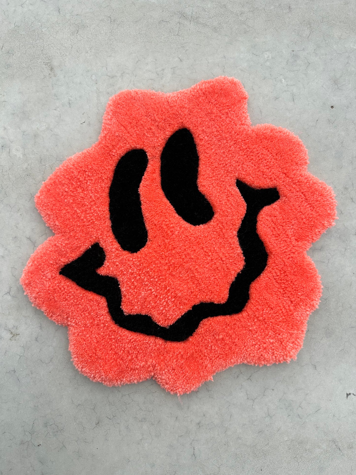 Shows our tufted TRIPPY Smiley Rug, it's a small orange hued smiley face with curvy edges and lines. Made by The Woollers