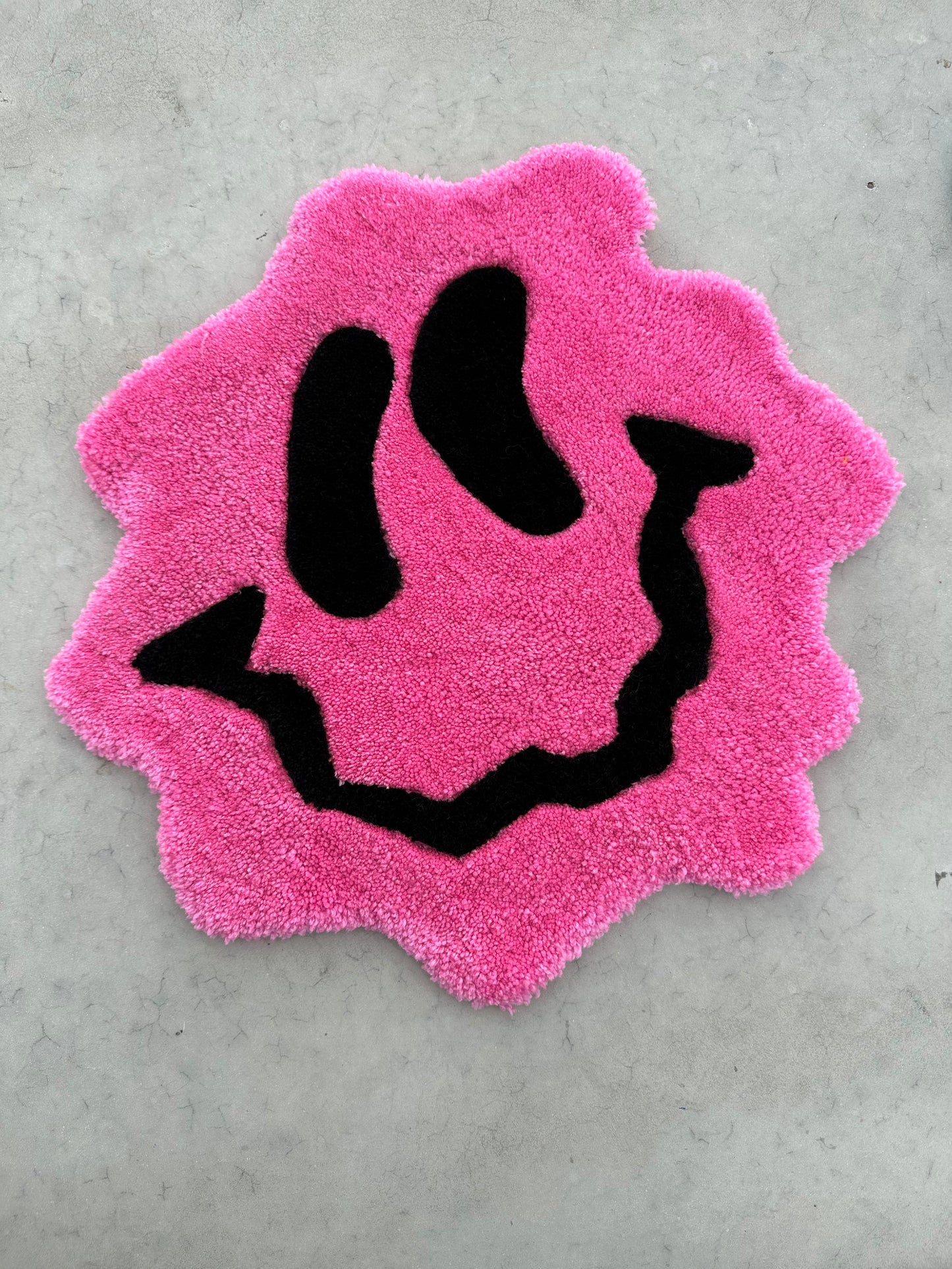 Shows our tufted TRIPPY Smiley Rug, it's a small pink hued smiley face with curvy edges and lines. Made by The Woollers